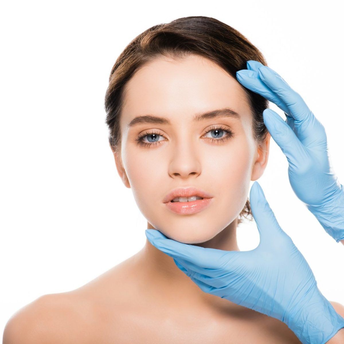 cropped view of plastic surgeon in blue latex gloves touching face of beautiful woman isolated on