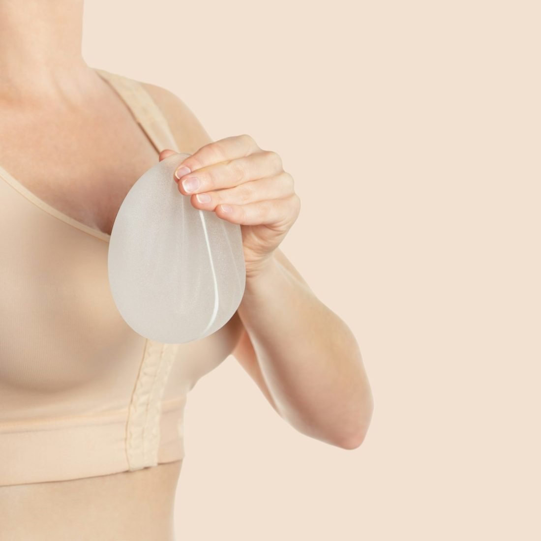 Woman wearing compressing bra after breast augmentation. Holding implants